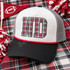 ND collegiate block letters DTF transfer filled with red, green, white, and black tartan plaid pattern and dark charcoal outline on a pink shirt Shown on a white front panel, black bill, grey mesh back, red rope trucker hat.
