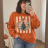 Fall DTF transfer featuring a layered pumpkin design with leopard print, harlequin, and polka-dot sections topped with an orange gingham bow on a tan polka-dot striped background Shown on a Orange crewneck sweatshirt.
