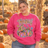 Thankful DTF transfer with hand-lettered script and a stack of watercolor-style pumpkins and squash in pink, orange, and blue with gold glitter accents, surrounded by stars Shown on a Heliconia crewneck sweatshirt.