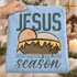 JESUS the reason for the season Christmas DTF transfer with hand-drawn nativity manger scene featuring a swaddled baby peeking over straw bedding Shown on a Ice Blue t-shirt.