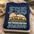 JESUS the reason for the season Christmas DTF transfer with hand-drawn nativity manger scene featuring a swaddled baby peeking over straw bedding Shown on a Sapphire crewneck sweatshirt.