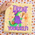 Treat Yourself Halloween DTF transfer with a green alligator dressed as a witch in a purple hat and cloak, holding a broom and jack-o-lantern pail, framed by orange stars on a retro striped background Shown on a Butter t-shirt.
