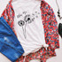 Blow Me Dandelion Sublimation Transfer, image of a white T-shirt with a dandelion design and text, surrounded by blue jeans, a floral jacket, black shoes, and accessories.