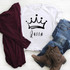 Queen Sublimation Transfer, graphic white T-shirt with a crown design and the word Queen on it, alongside denim jeans, a burgundy jacket, and brown boots, arranged on a white surface.