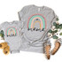 Mini Rainbow INFANT Screen Print Heat Transfer on matching gray T-shirts for mom and mini, with colorful rainbow design and script text, displayed alongside baby shoes, cotton flowers, and greenery.