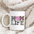 Mom Life patterned word art sublimation transfer on a white mug, featuring a pink lipstick kiss mark and leopard print letters, placed on a fluffy beige blanket.
