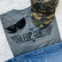 Top Dad Screen Print Heat Transfer, gray T-shirt with a black graphic design featuring the words 'Top Dad' and wings, accessorized with black sunglasses, a camouflage cap, and blue jeans on a white fluffy surface.