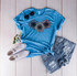 Patriotic Flag Sunflower Trio Screen Print Heat Transfer, blue t-shirt with sunflower design, paired with distressed denim shorts, white sneakers, and sunglasses, featuring patriotic colors and sunflower artwork.