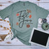 Fall for Jesus He Never Leaves Screen Print Transfer, autumn-themed t-shirt with fall leaves design and inspirational quote on a wooden background with pumpkins and decorative items.