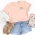 Hello Summer HAT/POCKET Screen Print Heat Transfer, casual summer outfit with pastel pink t-shirt featuring 'Hello Summer' print, denim shorts, beige sandals, and tropical patterned fabric.