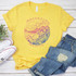 Adventure Awaits Watercolor Screen Print Heat Transfer, yellow t-shirt with landscape mountain and river design.