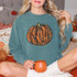 Leopard Orange Glitter Look Pumpkin Screen Print Heat Transfer, close-up of a woman wearing a teal sweatshirt featuring a glittery orange pumpkin with leopard print details, sitting on a cozy setting with pumpkins and fall decor.