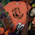 Just The Tip Screen Print Transfer, graphic design of a woman holding a sword with the words "Just The Tip I Promise" on an orange T-shirt, surrounded by Halloween decorations such as pumpkins, skull, witch's book, and dried flowers.