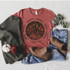 Sweaters Hayrides Boots Pumpkins Screen Print Transfer, flat lay of a fall-themed casual outfit featuring a graphic t-shirt with a bonfire and trees design, paired with denim jeans and ankle boots, surrounded by cozy sweaters, mini pumpkins, and a sprig of greenery.