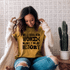 Well-Behaved Women Rarely Make History Screen Print Heat Transfer, a woman wearing a yellow t-shirt with the inspirational quote, sitting indoors with a cactus plant in the background.