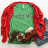 Gettin' Lit Screen Print Heat Transfer, festive holiday-themed green t-shirt with 'gettin' lit!' text and string of colorful Christmas lights, paired with a red cardigan, denim shorts, and holiday accessories.
