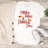 Chunky Thighs & Pumpkin Pies Sublimation Transfer on a white t-shirt, with a cozy cream knit cardigan and white sneakers with black accents, on a wooden surface with a small green plant nearby.