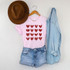 Red Hearts Metallic Screen Print Transfer, red glitter hearts design on a pink t-shirt with denim shorts, a brown hat, and a light blue denim shirt hanging on hanger.