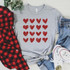 Red Hearts Metallic Screen Print Transfer, a grey t-shirt with red glittery hearts design laid out with a red and black checkered shirt, blue jeans, and white sneakers.