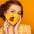 Lady Bug MASK/CAN HUGGER/POCKET Screen Print Heat Transfer, a yellow fabric face mask with a ladybug design on a polka dot background worn by a woman with red hair and blue eyes against an orange background.