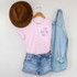 Oh Happy Day POCKET/MASK Screen Print Heat Transfer, pink t-shirt with colorful text, denim shorts, light blue denim shirt, and a brown felt hat hanging on a wall