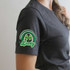 Lucky Rainbow POCKET/MASK Screen Print Heat Transfer, close-up of a person's shoulder showing a green rainbow and four-leaf clover design with the word Lucky on a dark gray t-shirt.