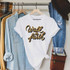 Walk By Faith Sublimation Transfer, white T-shirt with black and gold design hanging on a clothing rack.
