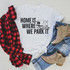 Home Is Where We Park It Sublimation Transfer, white T-shirt with a camper trailer graphic and text, paired with ripped blue jeans, a beige ankle boot, and a red plaid shirt, arranged on a beige textured surface.