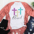 Truly Blessed Sublimation Transfer, T-shirt featuring colorful cross design and "Truly Blessed" text with a pink cardigan, black boots, and distressed jeans on a white wooden background.
