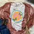 Good Things Take Time Sublimation Transfer, colorful T-shirt with peace sign and butterfly design, laid on pink lace cardigan with denim jeans and beaded bracelets.