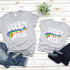 Lucky Mini Rainbow Screen Print Heat Transfer t-shirts, grey casual shirts with rainbow design and white 'LUCKY' text, laid on wooden surface with jeans and a small green plant.