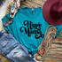 Hippie Mama Screen Print Heat Transfer, turquoise t-shirt with Halloween-inspired typographic design, surrounded by colorful accessories including beads, a maroon hat, earrings, and decorative feathers.