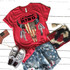 Patriotic Skull Screen Print Heat Transfer, red t-shirt with a skull design featuring an American flag pattern and the words "Let Freedom Ring". The outfit is styled with distressed denim shorts with star patterns, white sneakers with black stripes, and patriotic accessories including a flag pin and a woven clutch with fringe accents.
