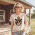 Cowboy Smile Screen Print Heat Transfer, cheerful cow face design with cowboy hat on a white t-shirt worn by a smiling woman outdoor scene.