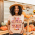 Fall That Beautiful Time Of The Year DTF Heat Transfer, woman wearing a beige t-shirt with fall-themed text and pumpkins, autumn pumpkin display setting.