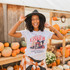 We're Going Witchin' Screen Print Heat Transfer, woman wearing Halloween-themed graphic t-shirt with pumpkins in the background.