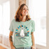 Let The Spooky Times Roll DTF Transfer, image of a woman wearing a light green T-shirt with a ghost skateboarding and colorful text design