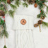 Custom Initial TAN Leather Patch, cream knitted winter scarf with a monogrammed leather patch featuring the letter 'K' on a white fluffy surface surrounded by pine branches and pine cones for Christmas decoration.