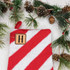 Custom Initial TAN Leather Patch You Choose Style and Text, product image of a personalized tan leather patch with an initial 'H' placed on a red and white striped Christmas stocking, surrounded by pine branches and pinecones.