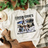 Cousin Eddie Septic Services Screen Print Transfer, humorous graphic t-shirt featuring a cartoon of a woman by a septic tank and an RV, with the text 'Cousin Eddie's Septic Services, Cleaning out shitter since 1989' on a white sweatshirt, laid on a cozy blanket with holiday decor.