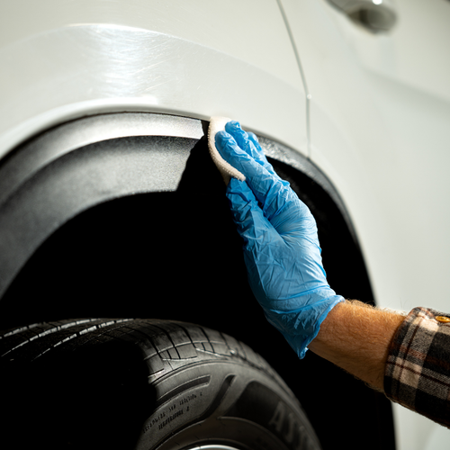 Person applying Wipe New Trim Restore to black fender trim on white vehicle for restoration and protection