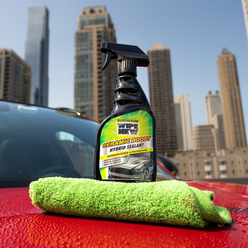 Wipe New Ceramic Boost Hybrid Sealant displayed on red car hood with green microfiber towel and city skyline background
