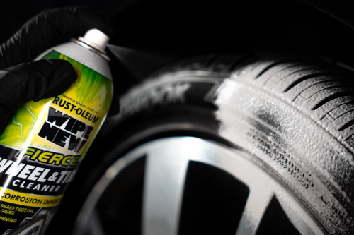 A hand holding a Rust-Oleum Wipe New cleaner spray can, spraying a tire with foam.