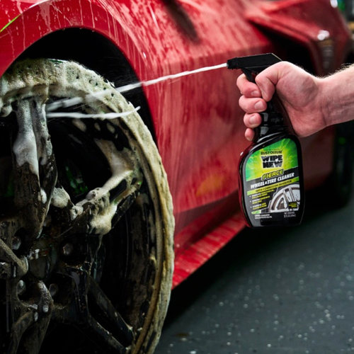 A hand holding a bottle of Rust-Oleum wheel and tire cleaner, spraying foam on a car wheel.