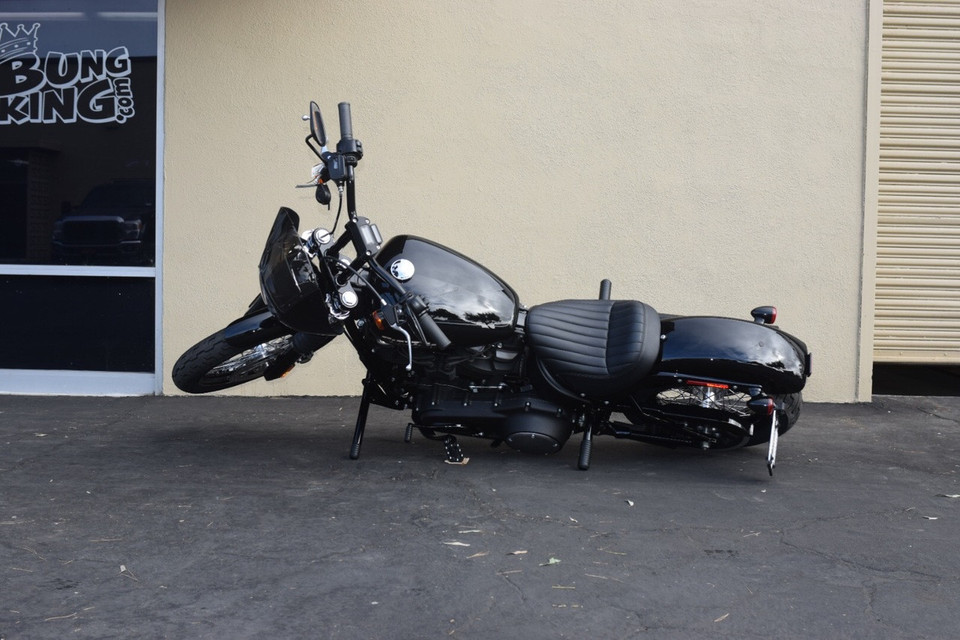 Passenger peg crash bar frame slider on Harley M8 Softail (2018-2025) with bike laid over showing protection from tip-over, replaceable Delrin puck, gloss black finish FXLRS