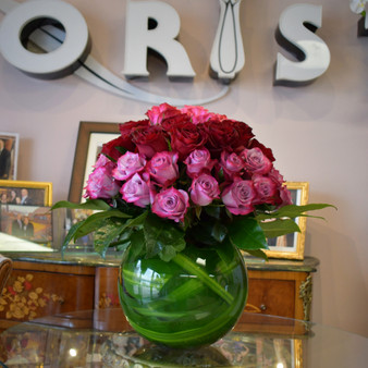 Sending My Love is a luxury red and lavender rose arrangement in green glass bowl by Lexis Florist in Houston. Round green glass bowl vase, filled with two-tone roses, with lush greenery.