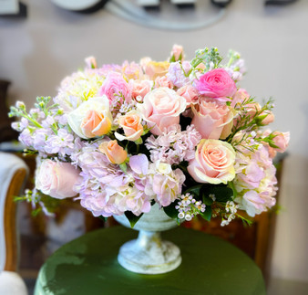 Lady in Bloom is a soft, feminine, upscale, garden-party elegant arrangement featuring blush peach roses, pink hydrangeas, soft pastel accent blooms, arranged in  white pedestal compote vase, a very romantic garden style handcrafted by Lexis Florist Houston