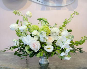 Elegant Purity is a clean, luxurytimeless  arrangement featuring white roses, white orchids, white ranunculus and similar soft blooms, green hydrangea accents, and lush greenery arranged in a silver pedestal compote vase handcrafted in Houston  by Lexis Florist