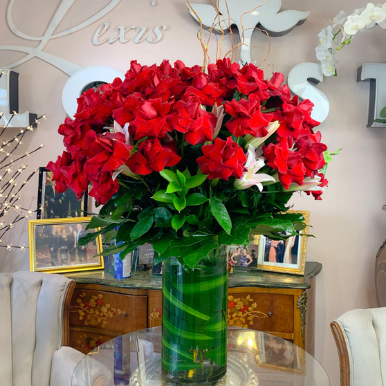 Blooming Poem is a large luxury arrangement dominated by signature red roses mixed with white lilies with and lush green foliage, arranged in  tall glass cylinder vase  by Lexis Florist Houston