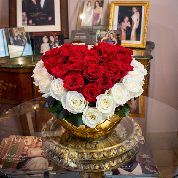 A heart shaped flower arrangement or roses red and white.